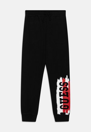 Pantalones deportivos negros con puños y cintura elásticos, con un diseño de pinceladas blancas y rojas y la palabra "GUESS" impresa en la parte inferior de la pierna.