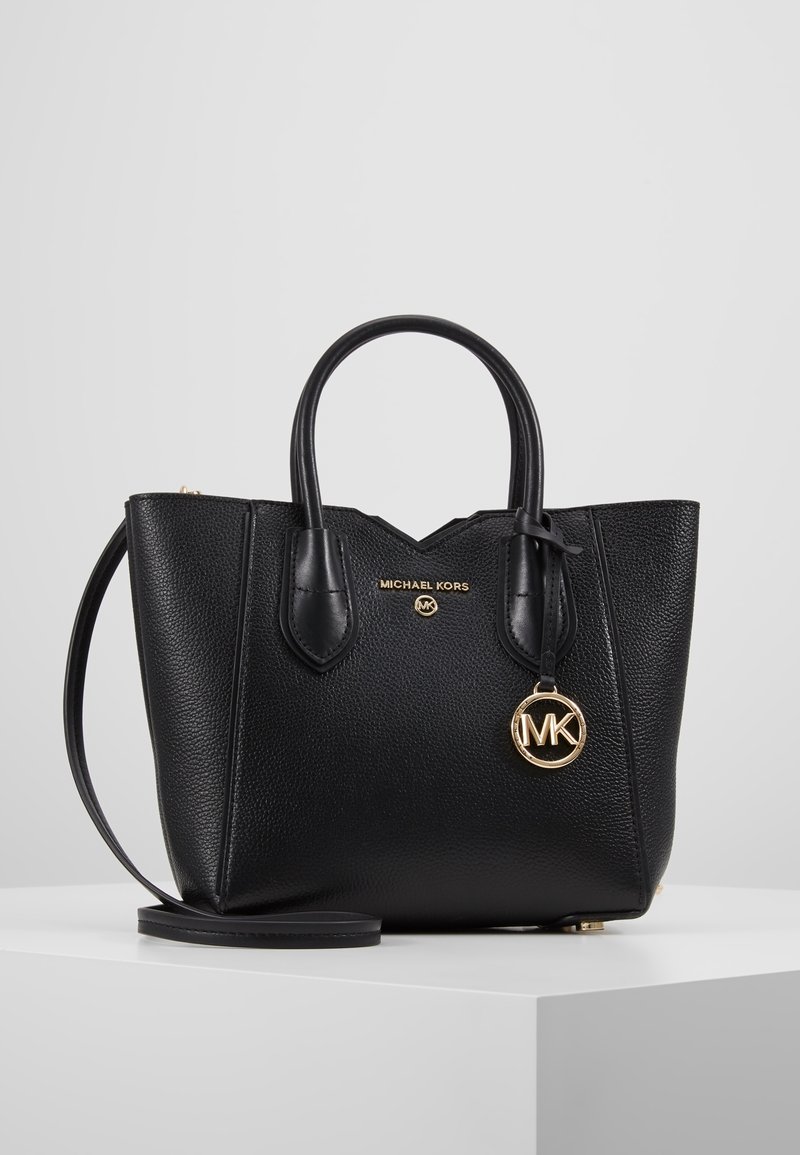 Sac à main Michael Kors en cuir noir texturé avec double poignée, breloque logo dorée et bandoulière amovible sur surface blanche.