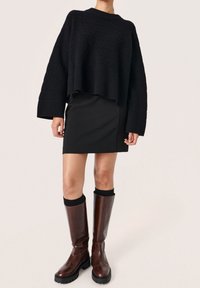 Czarny sweter dzianinowy z szerokimi rękawami, zestawiony z czarną dopasowaną spódnicą oraz ciemnobrązowymi skórzanymi botkami do kolan z grubą podeszwą.