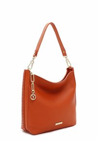 Sac à main en cuir orange rouille avec surface texturée, breloque en chaîne en or et bandoulière simple, présenté en angle sur fond blanc.