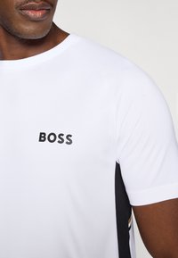 Λευκό κοντομάνικο T-shirt με μαύρο λογότυπο "BOSS", διαθέτει στρογγυλή λαιμόκοψη και μαύρες πλαϊνές λεπτομέρειε�ς για αντίθεση και υφή.
