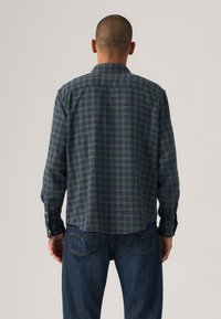 Checks-pattern shirt in dark green and blue, featuring a collared neck, long sleeves, and buttoned cuffs; made of lightweight fabric.