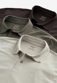 Tres camisas polo en varios colores: marrón oscuro, verde oliva y beige claro. Todas tienen cuellos abotonados y un pequeño logo en el frente.