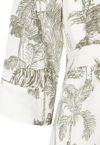 Tissu blanc avec des illustrations de palmiers verts et de tigres, comportant des textures détaillées. Le design couvre les manches et le corps du vêtement.