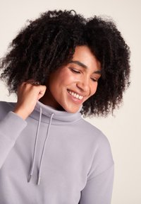 Light purple sweatshirt with a high collar, drawstrings, and ribbed cuffs. Soft, textured material with a relaxed fit.