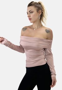 Schulterfreies Oberteil mit langen Ärmeln aus weichem rosa Stoff mit Rüschendetails. Kombiniert mit schwarzen, eng anliegenden Hosen, die eine schlanke Silhouette betonen.