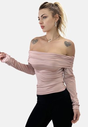 Schulterfreies Oberteil mit langen Ärmeln aus weichem rosa Stoff mit Rüschendetails. Kombiniert mit schwarzen, eng anliegenden Hosen, die eine schlanke Silhouette betonen.
