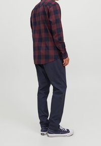 Camicia a righe rossa e blu, abbinata a pantaloni blu scuro e sneakers blu. La texture appare liscia, con uno stile casual.