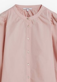 Lichtroze katoenen shirt met een ronde hals, pofmouwen en een knoopsluiting aan de voorkant. Heeft kleine, glanzende knopen langs de overslag.