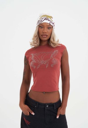Rood kraagloos crop top met een versierde uitstraling met bloem- en kreeftenmotieven. Model draagt een zwarte denim rok en een gestreepte witte beanie.