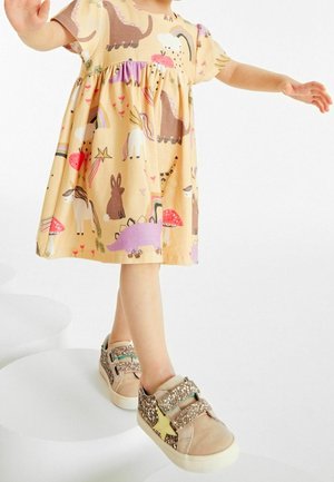 Robe à manches courtes, de couleur jaune clair, ornée de motifs d'animaux et d'arc-en-ciel. Baskets marron et beige avec des accents pailletés et un motif d'étoile.