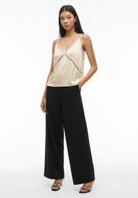 Sateng-kamisol i krem med blonderdetaljer, med tynne stropper. Kombinert med høytlivs svarte bukser med vide ben. Svarte hæler med stropper.