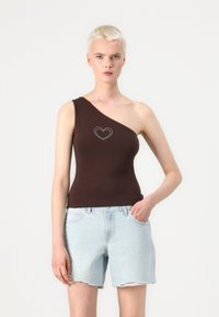 Rjava enoramna top s tankom in srcem iz kovinskih žebljev na prsih. Uporabljena z svetlo modrimi jeans kratkimi hlačami, ki imajo raztrgano rob.