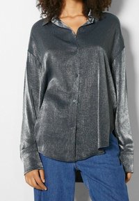 Grå metallisk knäppskjorta med lös passform, långa ärmar och en rundad nederkant, med en subtil lyster och en klassisk kragdesign.