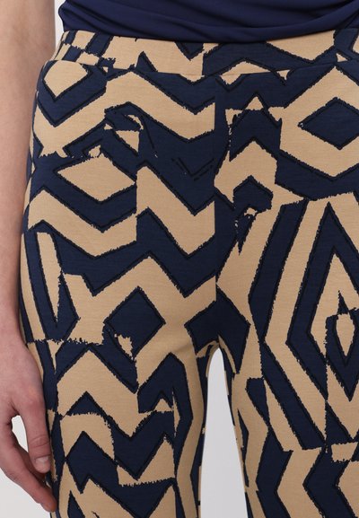 Marineblå og beige leggings med mønster, der har et zigzag-design med teksturerede detaljer, fremstillet af et fleksibelt stof for komfort.
