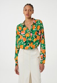 Bloes met bloemenmotief met levendige oranje en roze rozen op een groene achtergrond, met een knoopsluiting en lange mouwen.