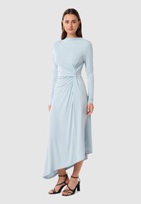 Light blue long-sleeve dress with draped fabric, a twisted front detail, and an asymmetrical hem. Smooth texture, made from a stretchy material.