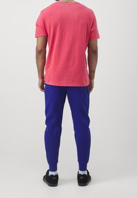 Rotes Baumwoll-T-Shirt und blaue Jogginghosen mit schlankem Schnitt und elastischem Bund, kombiniert mit schwarzen Schuhen und weißen Socken.