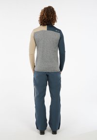 Grijze, beige en marineblauwe lange mouw top met een half-rits ontwerp. De stof is textuurgevoelig. Gepaard met blauwe broeken met zijritsen.