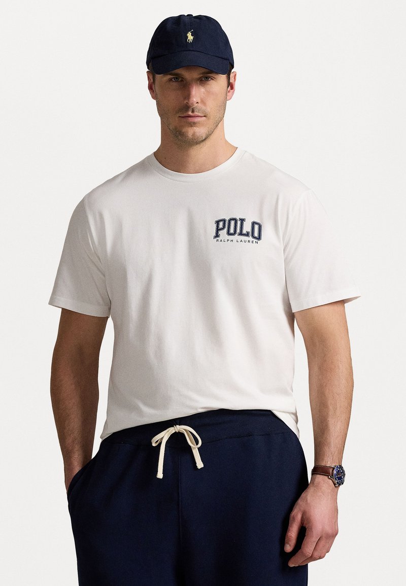 Balta medvilninė marškinėliai su mėlyna spalva užrašyta "POLO RALPH LAUREN". Derinama su mėlynomis sportinėmis kelnėmis, turinčiomis elastingą juosmenį ir raištelį.