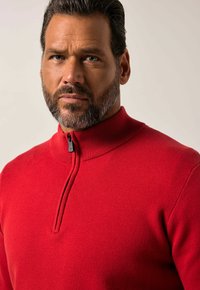 Roter Sweater mit Reißverschluss und geripptem Kragen, der ein strukturiertes Strickmuster und ein dezentes Zipper-Detail am Kragen aufweist.