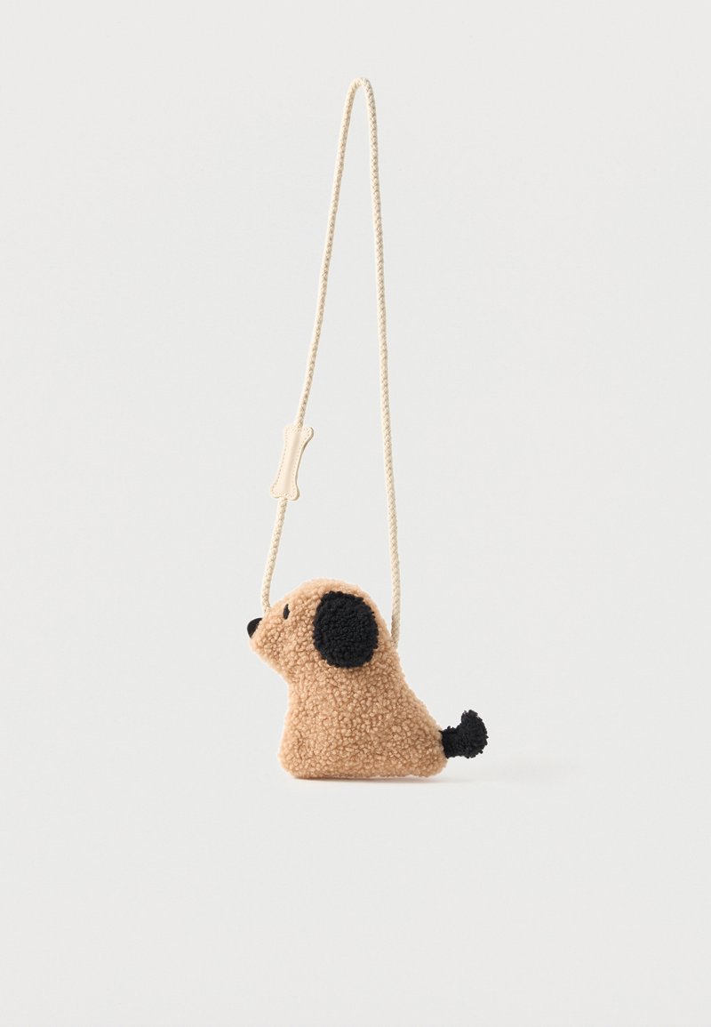 Μικρό μπεζ τσαντάκι crossbody από βελούδο σε σχήμα σκύλου με μαύρα αυτιά, μύτη, ουρά και μακρύ κρεμ λουράκι με λεπτομέρεια σε σχήμα κόκαλου.