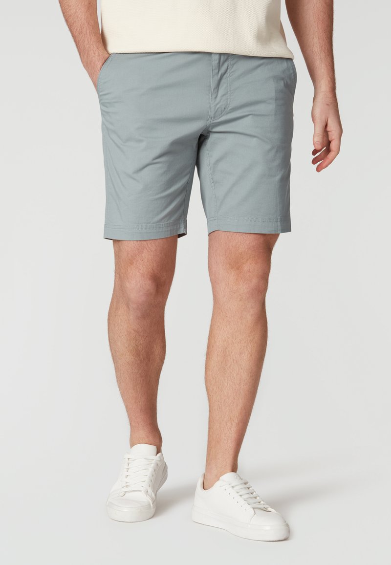 Shorts en coton gris avec une coupe plate, des poches latérales et une coupe régulière, associés à des baskets blanches sur un fond neutre.