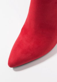 Stivale alla caviglia in suede rosso con punta affusolata e texture liscia, con tacco alto e silhouette elegante.