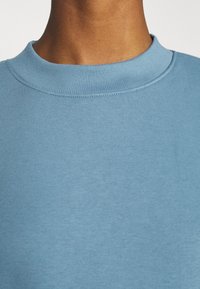 Sweat-shirt bleu clair avec un col rond côtelé. Le tissu semble lisse et doux, avec des coutures minimales et sans logos ni motifs visibles.
