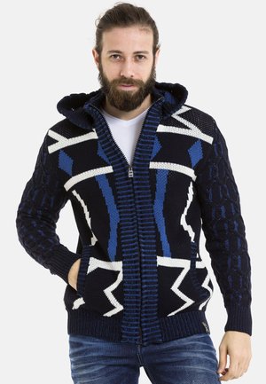 Strick-Hoodie-Cardigan in Marineblau mit blauen und weißen geometrischen Mustern, einem Frontreißverschluss sowie gerippten Bündchen und Saum. Strukturierte Ärmel.