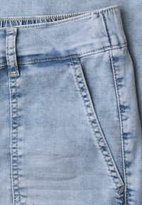 Zbliżenie na jasnoniebieskie dżinsy z denimu, pokazujące pas, pętlę na pasek i przednią kieszeń z widocznymi detalami szwów.