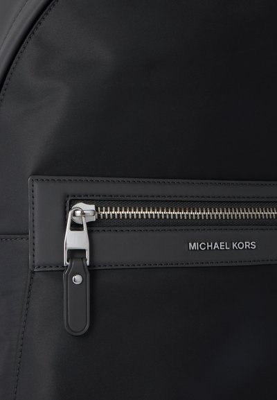 Poche noire avec fermeture éclair argentée et languette noire, avec le nom de marque Michael Kors embossé en lettres argentées.