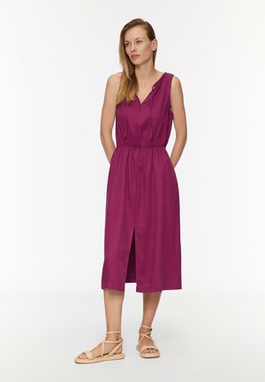 Magenta ärmelloses Kleid mit V-Ausschnitt und kontrastierbarem Taillenband. Es hat einen Beinschlitz und eine glatte Textur. Kombiniert mit hellbraunen flachen Sandalen.