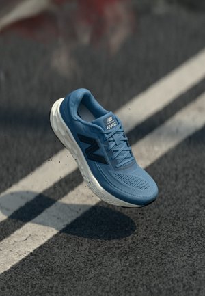 Baskets de course bleu clair avec dessus en maille texturée, accents bleu foncé et semelle intermédiaire blanche, présentées au-dessus d'une surface routière avec des lignes peintes.