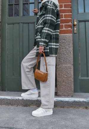 Chaqueta grande de cuadros verdes y blancos, pantalones beige claro, zapatillas blancas con rayas multicolores y un pequeño bolso marrón.