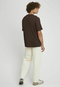 Chemise à manches courtes texturée marron, pantalon large blanc et baskets à motifs ; modèle vu de dos contre un fond uni.