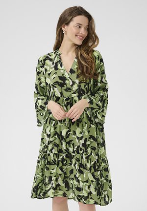 Grünes gemustertes Kleid mit V-Ausschnitt, langen Glockenärmeln und einem gestuften Rock. Der Stoff hat eine glatte Textur mit einem Mix aus dunklen und hellen Grüntönen.