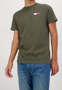Bavlněné tričko olivově zelené barvy s kulatým výstřihem, krátkými rukávy a malým značkovým logem s červenými, bílými a modrými pruhy na přední straně.