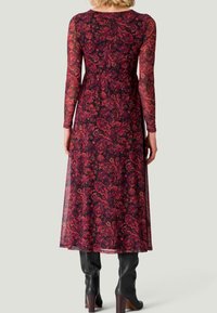 Långärmad klänning i genomskinligt burgundy tyg med blommönster och paisleymönster. Utsvängd silhuett och lätt transparent i fållen. Svarta knähöga stövlar.