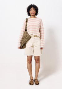Gestreifter rosa-weißer Strickpullover, beiger Shorts mit fransigen Kanten, Umhängetasche im Leopardenmuster und braune Sandalen mit Riemendetails.