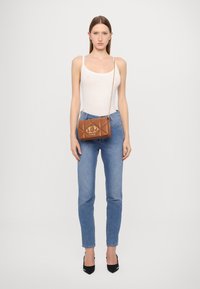 Borsa a tracolla in pelle marrone trapuntata con dettaglio hardware in oro con logo. Presenta una sottile tracolla a catena e una forma rettangolare.