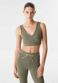 Olijfgroene sportbh met een diepe V-hals en brede banden, gecombineerd met bijpassende high-waisted leggings met een koord in de taille.