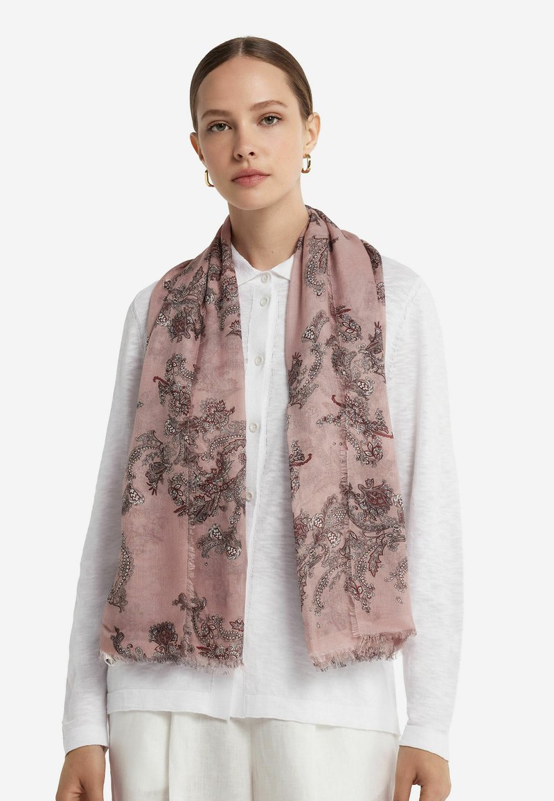 Écharpe rose ornée de motifs floraux complexes en noir et rouge, fabriquée dans un matériau léger avec des bords frangés. Portée sur un haut blanc.