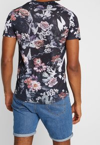 Camiseta negra de manga corta con un estampado floral que presenta flores rosas y blancas; tejido mezclado con una textura suave. Se lleva con pantalones cortos de denim.