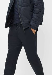 Giacca invernale nera con design trapuntato, chiusura con zip e tasche laterali, abbinata a pantaloni neri con vita elasticizzata e coulisse.