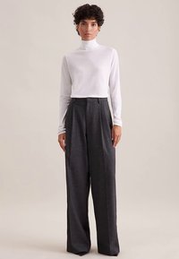 Dolcevita bianco a maniche lunghe abbinato a pantaloni grigio scuro a vita alta e gamba larga. I pantaloni presentano pieghe frontali e una vestibilità sartoriale.