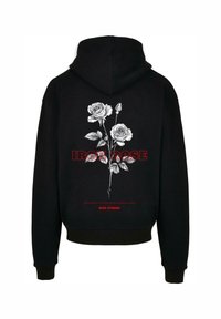 Must musta, mille seljal on valge roosi grafika, punase tekstiga "IRON ROSE" ja "RISE STRONG", pehmest struktuurse tekstuuriga kangast.