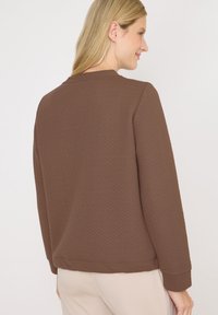Felpa marrone con texture, maniche lunghe e scollatura rotonda, caratterizzata da un sottile motivo geometrico e bordi a coste sui polsini e sull'orlo.