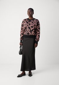 Črn pulover s cvetličnim vzorcem v rožnatih tonih, v kombinaciji z elegantno črno krilo. Dodatki vključujejo majhno črno torbico in ravne čevlje.