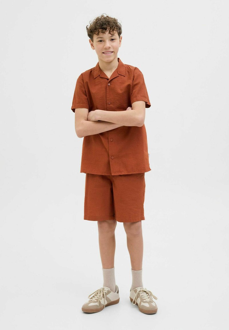 Rostfärgad kortärmad skjorta och matchande shorts i en strukturerad tyg. Outfitten har en avslappnad och ledig passform och är parat med ljusa sneakers.